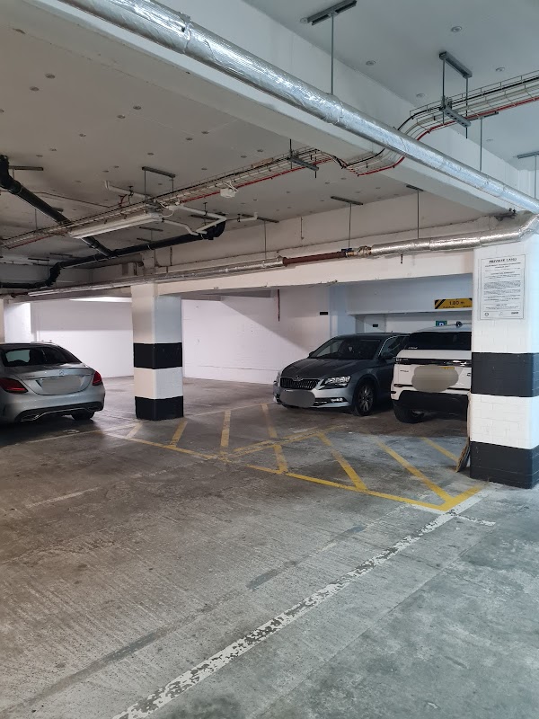 Empty parking area with two parked cars, concrete flooring, and overhead pipes in a well-lit garage.