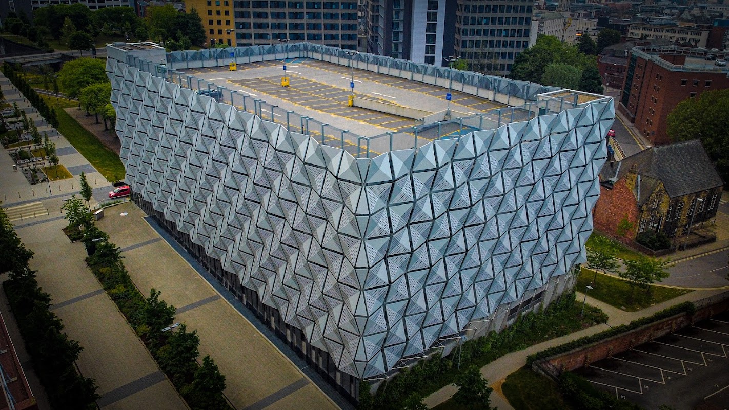Modern multi-story car park with a geometric façade, surrounded by greenery and urban buildings in Leeds, Yorkshire.