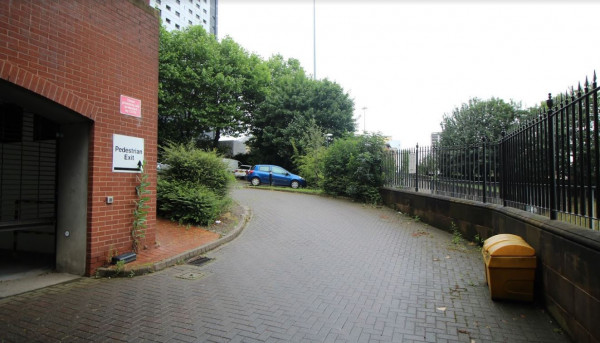 Pay & Display parking area in Leeds with a winding path, greenery, and a yellow bin near the pedestrian exit.