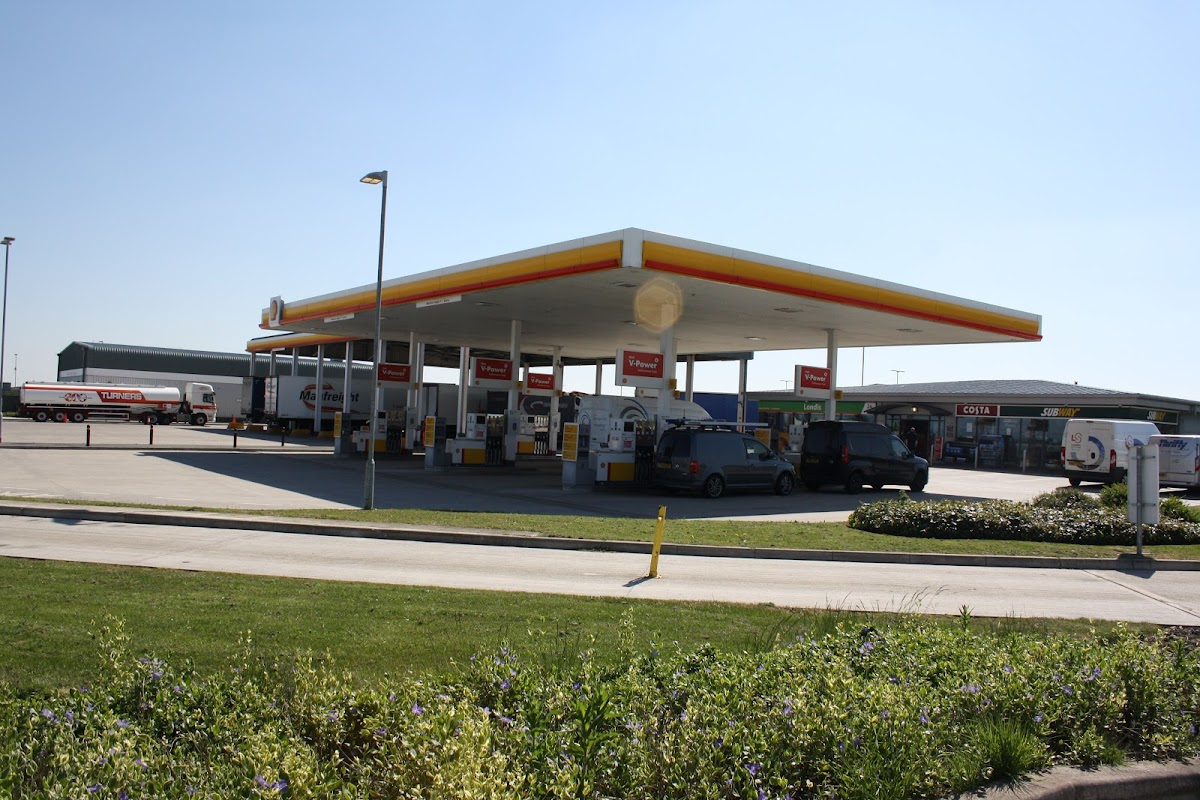 Gas station with multiple fuel pumps, trucks parked, and clear blue sky in the background.