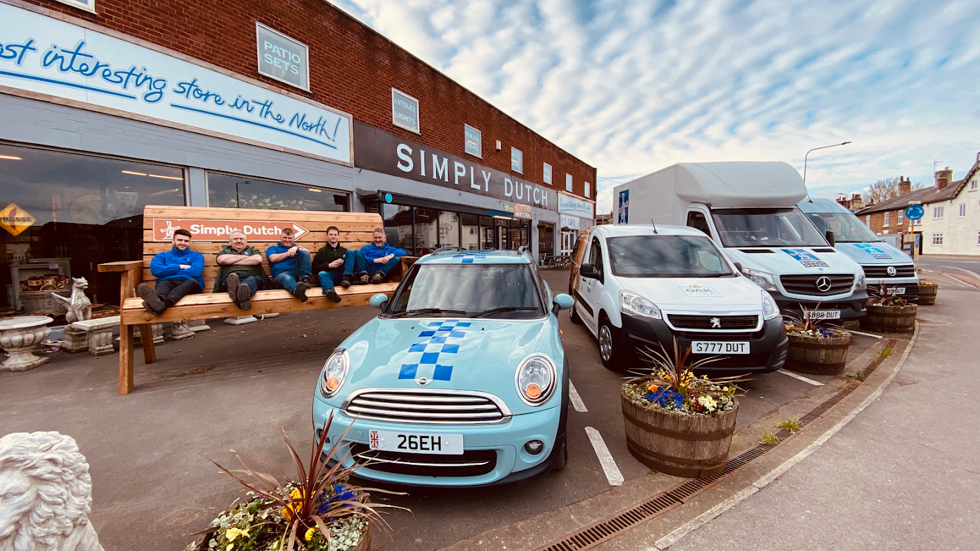 Blue and white shopfront of Simply Dutch, with staff sitting on a bench and delivery vans parked outside.