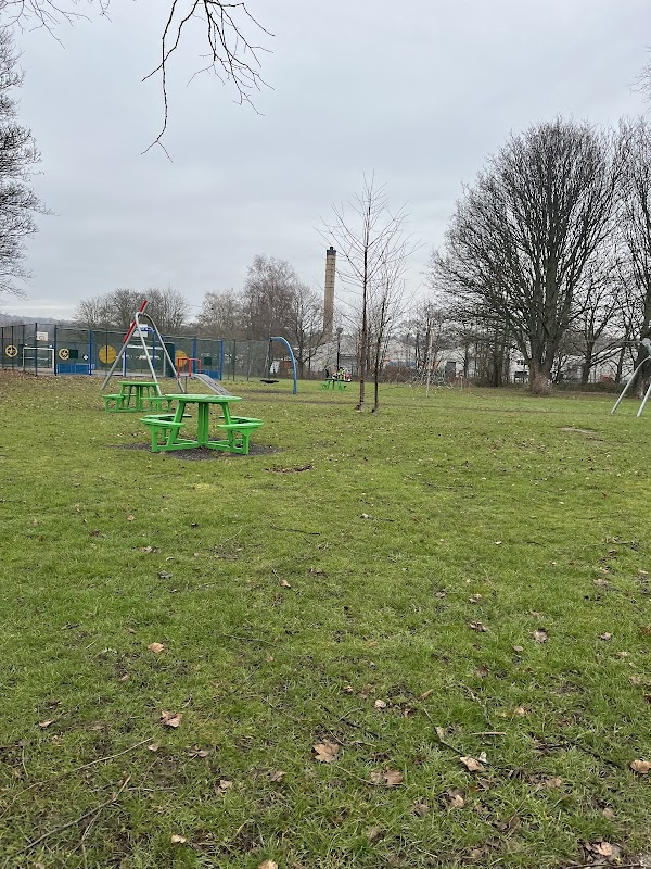 Green picnic tables on grass with playground equipment and trees in Darton Park, Mapplewell, Yorkshire.