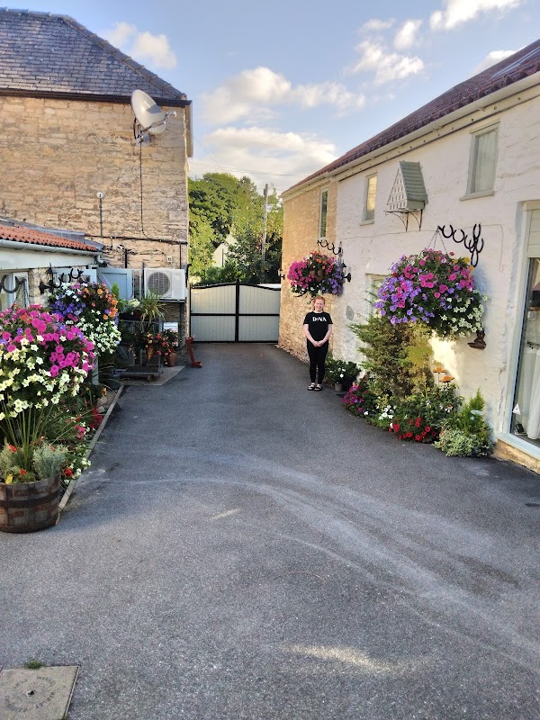 Charming courtyard of The Barn hotel, featuring vibrant flower baskets, stone walls, and a welcoming entrance.