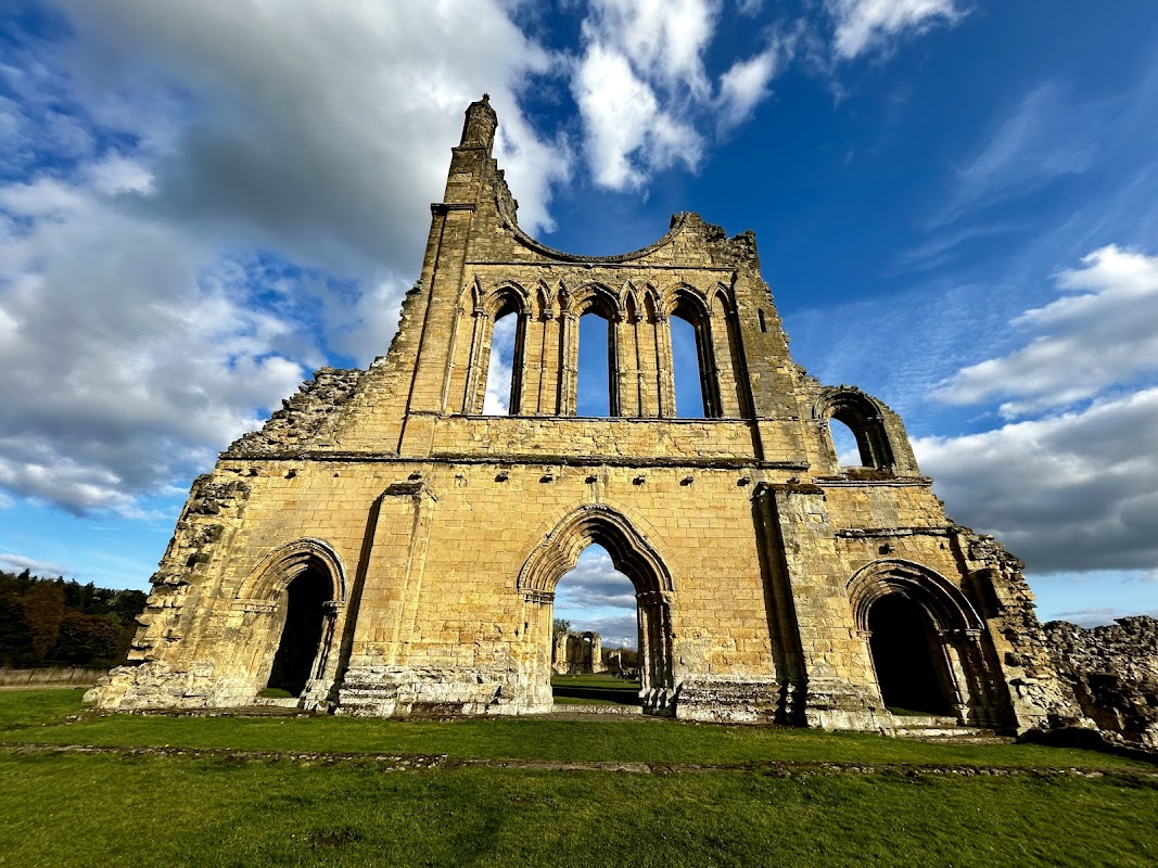 Ruins of Byland Abbey with tall stone walls, arched windows, and a dramatic sky in Newburgh, North Yorkshire.