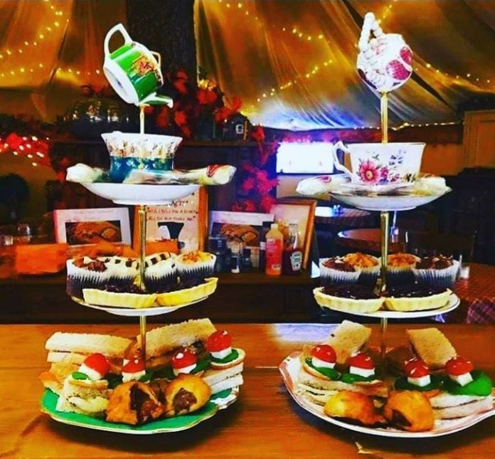 Tiered trays with sandwiches, scones, and cupcakes inside a cozy North Shire cafe adorned with warm fairy lights.