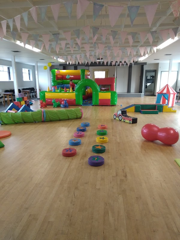 Brightly colored inflatable play equipment in a spacious hall, decorated with bunting and soft play areas.