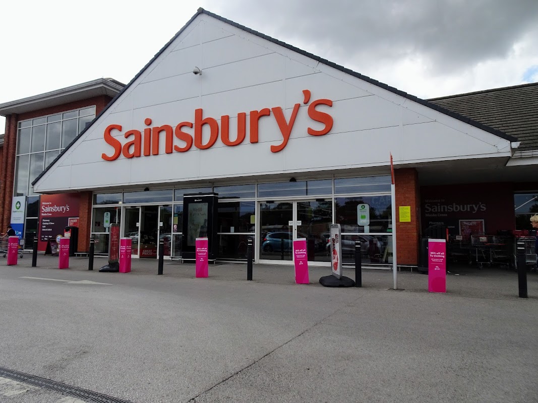 Sainsbury's storefront in Otley, Yorkshire, featuring large orange signage and pink promotional stands outside.