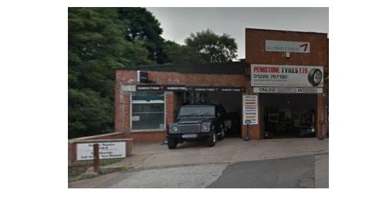 Penistone Tyres Limited garage with a black vehicle parked outside and signage displaying contact information.