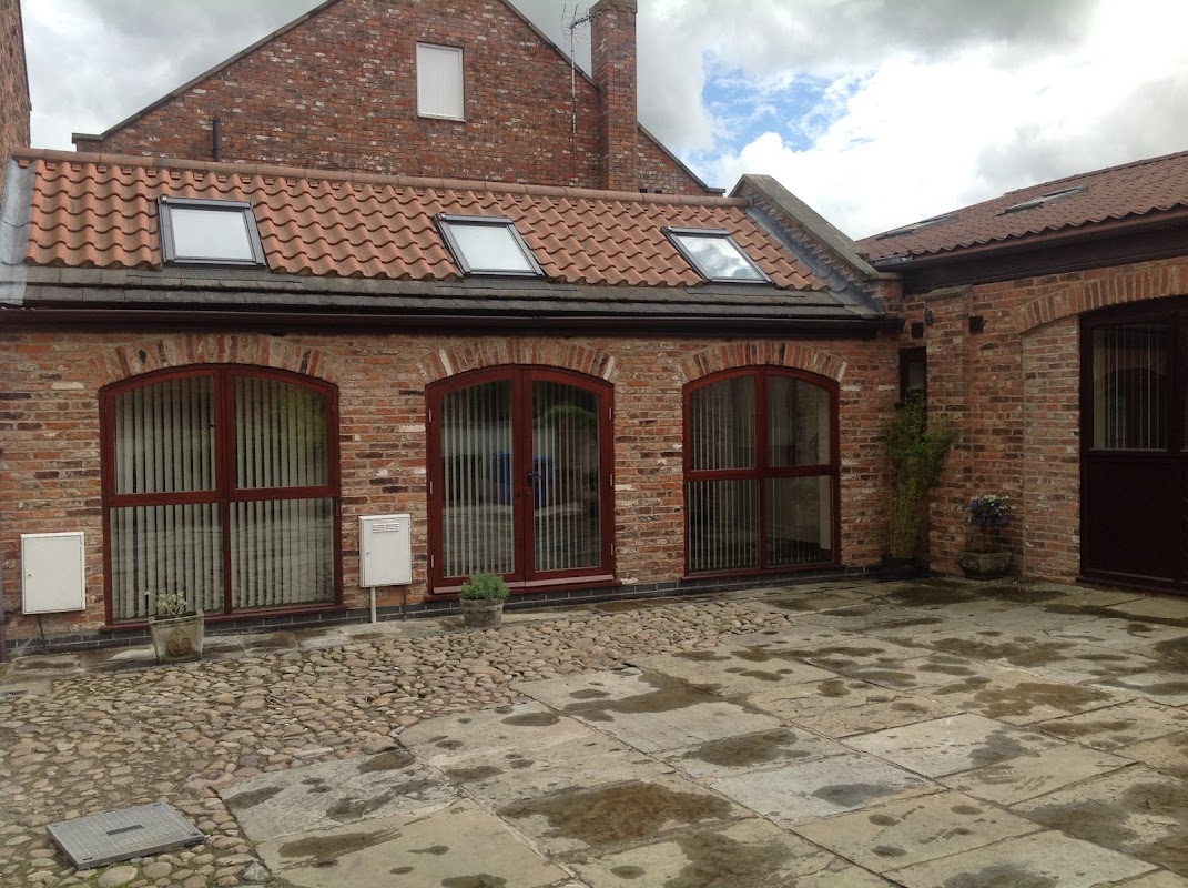 Red-brick guest house with arched windows, slate roof, and a stone-paved courtyard under a cloudy sky.