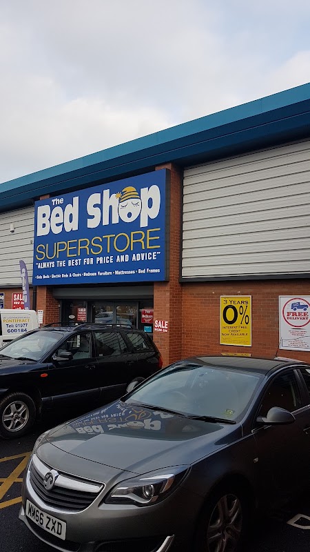 The Bed Shop Superstore storefront with blue signage, parked cars, and promotional sale signs.