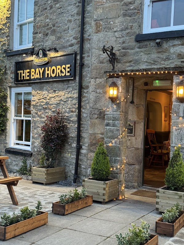 Stone exterior of The Bay Horse pub with warm lighting, wooden seating, and planters outside the entrance.
