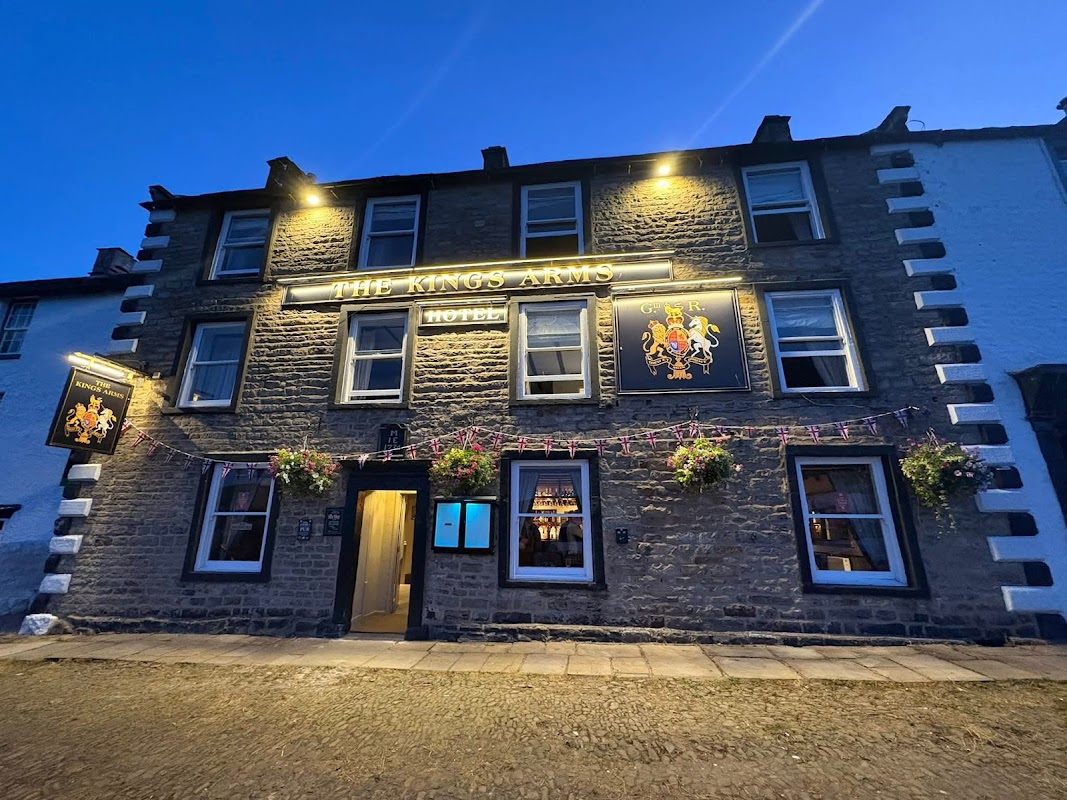 The Kings Arms Hotel in Reeth, Yorkshire, with illuminated signage and flower baskets on a stone facade at dusk.