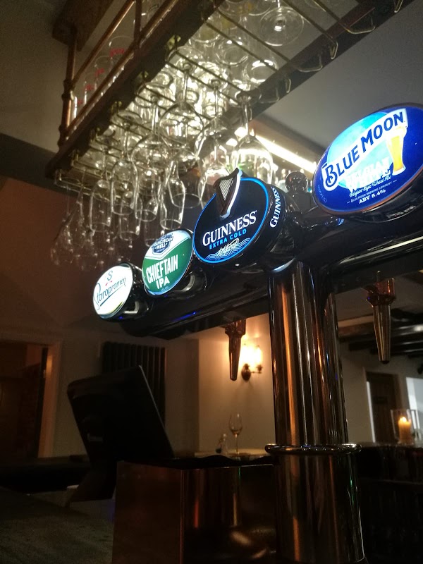 Bar counter with various beer taps, including Guinness and Chieftain IPA, and hanging glasses in the background.
