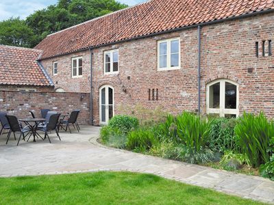 Woldsend Holiday Cottages features a brick building with a patio, outdoor seating, and lush greenery in Rillington, Yorkshire.