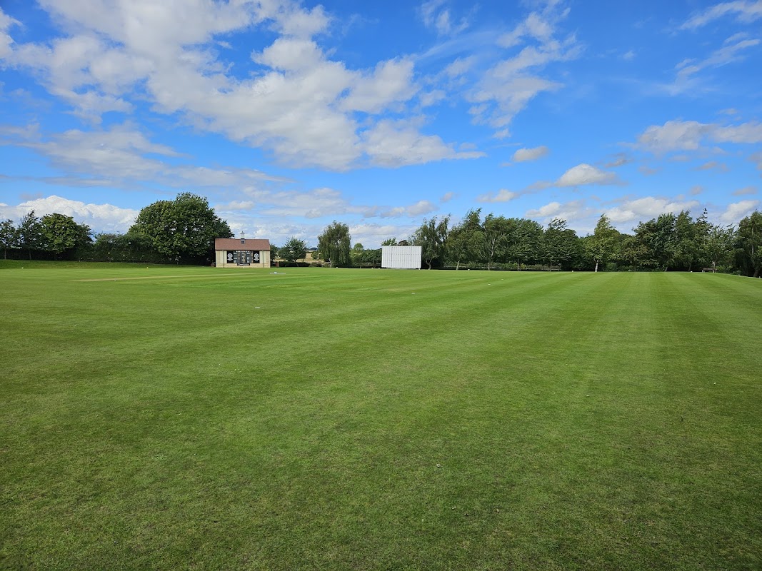 Cricket field with a clubhouse and scoreboard under a blue sky with scattered clouds in Saxton, North Yorkshire.