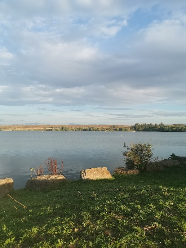 Calm water of Scaling Reservoir surrounded by greenery and rocky outcrops under a partly cloudy sky.