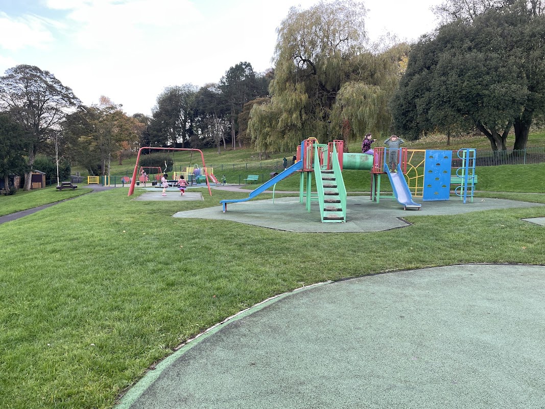 Colorful playground equipment with slides and climbing structures in a grassy park setting. Trees in the background.