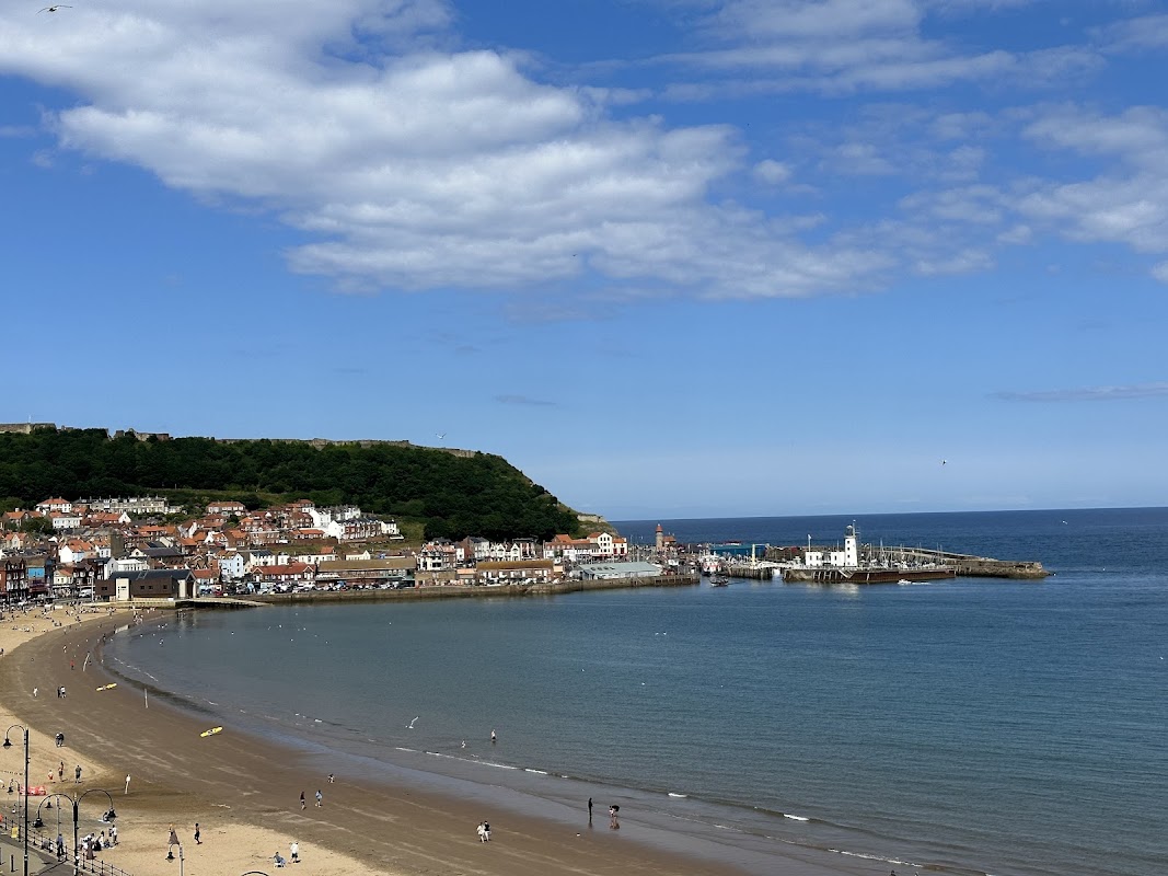 Scarborough's South Bay with sandy beach, colorful buildings, and a pier under a clear blue sky.