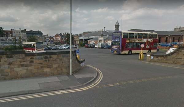 A busy car park in Scarborough with parked cars, a bus, and a mix of buildings in the background under a cloudy sky.