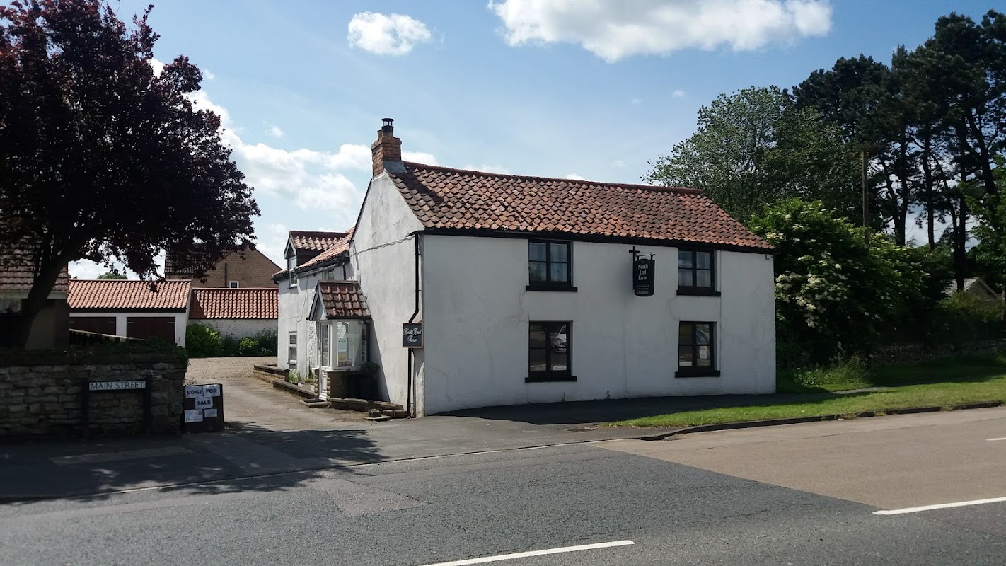 White cottage-style guest house with a red tiled roof, surrounded by greenery and a clear blue sky.