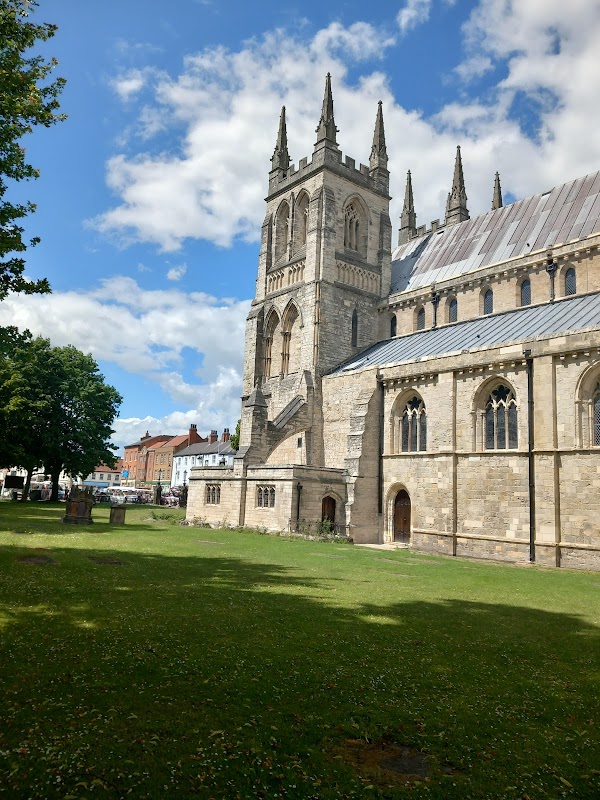 View of Selby Park with a historic church tower, green grass, and blue sky with scattered clouds.