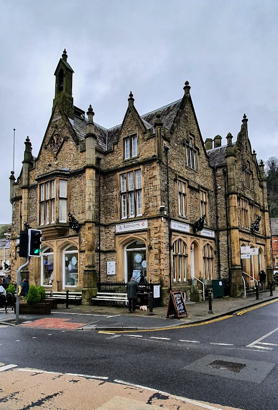 Victorian-style building with stone façade, decorative gables, and signage for bathrooms, set in a town square.