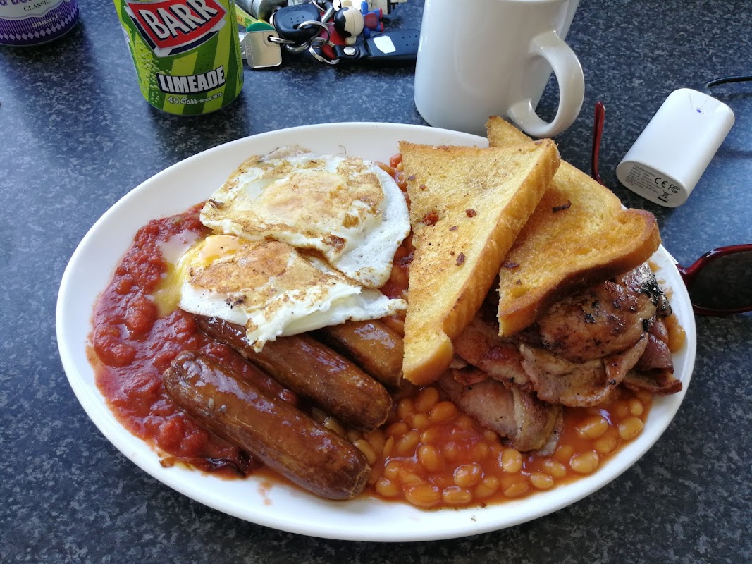 A hearty breakfast plate with sausages, eggs, baked beans, toast, and bacon, alongside a drink and keys.
