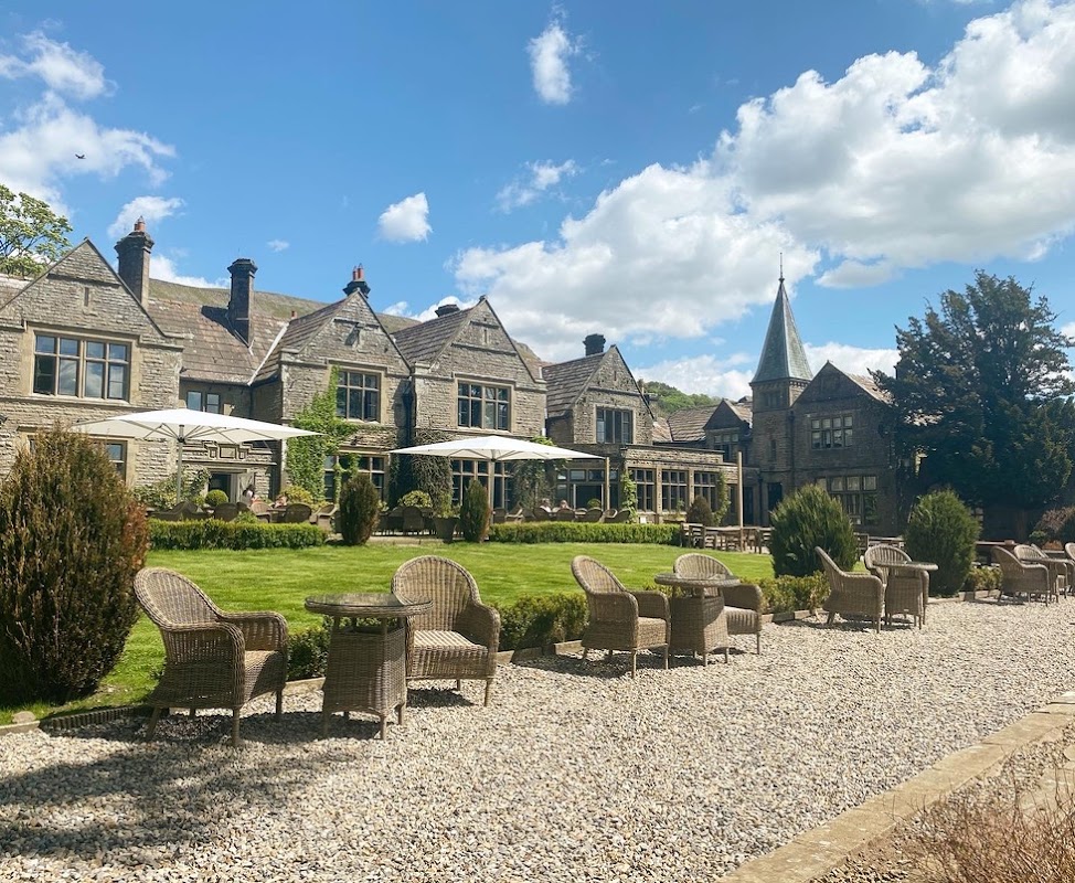 Stone building with a turret, outdoor seating, and lush green lawn under a blue sky with fluffy clouds.