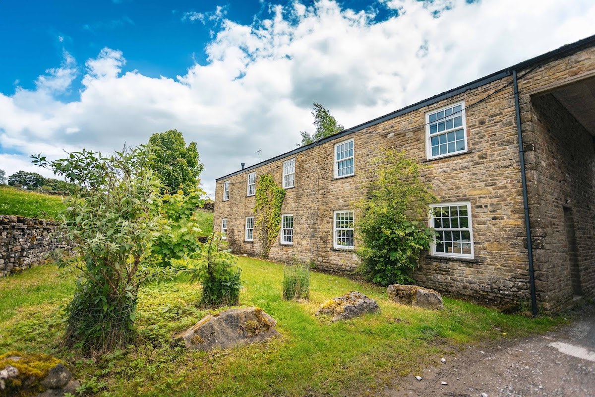 Stone building with large windows, surrounded by greenery and a blue sky with clouds in Simonstone, North Yorkshire.