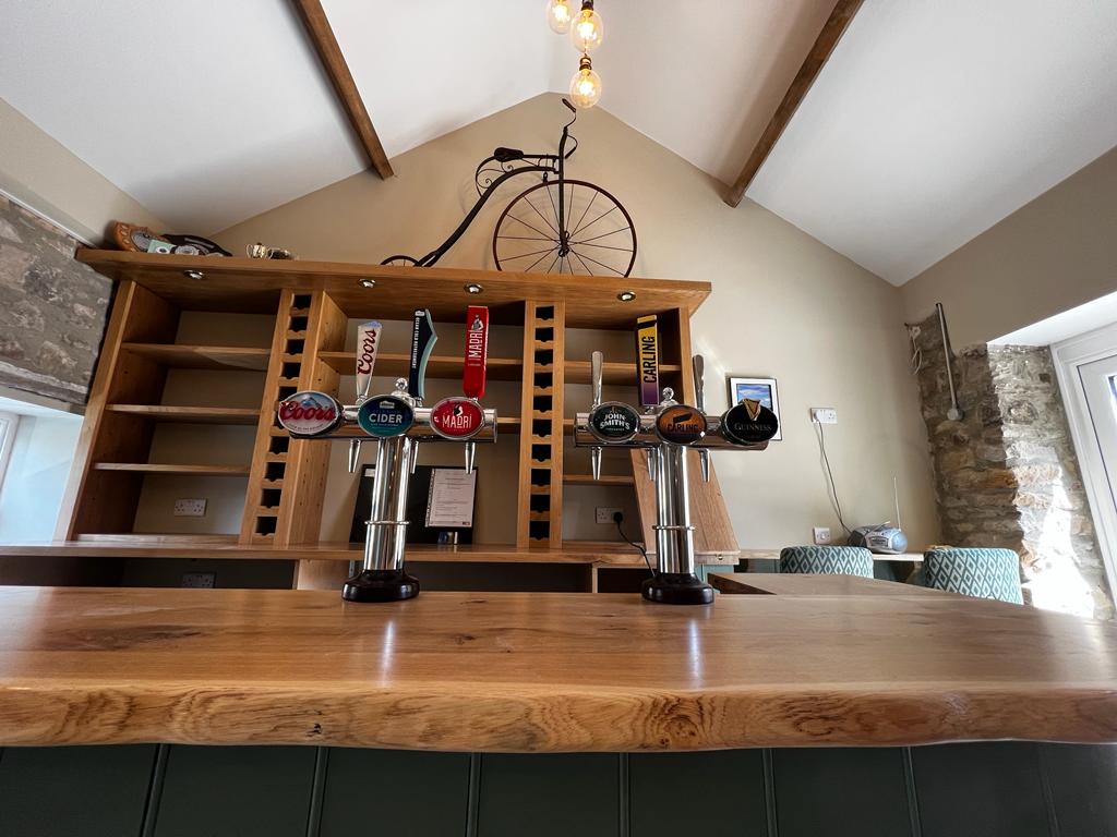 Bar counter with various beer taps, wooden shelves, and a vintage bicycle hanging from the ceiling in a cozy setting.