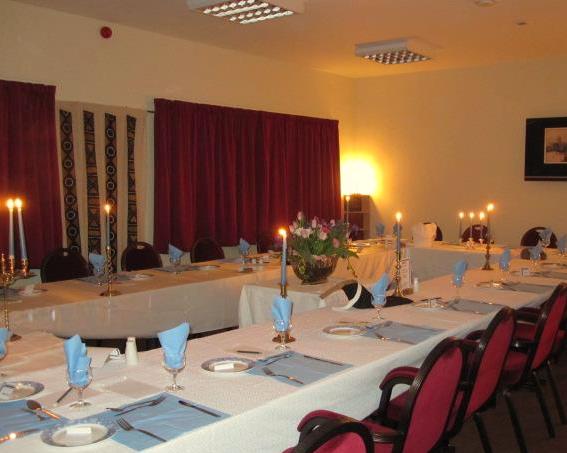 Elegant dining setup with blue napkins, candles, and floral centerpiece in a warmly lit hall. Red curtains in the background.