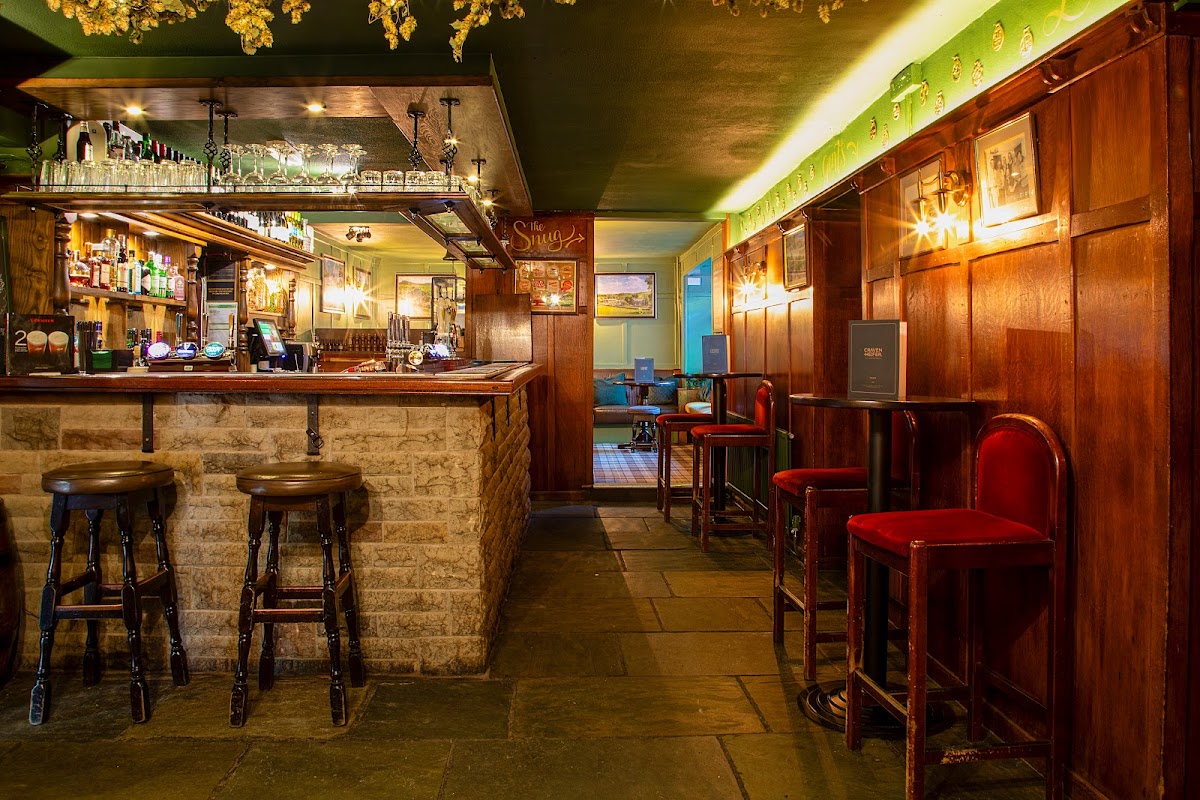 Warm wooden interior with a bar, stools, and dim lighting, creating a cozy atmosphere in Craven Heifer, Stainforth.