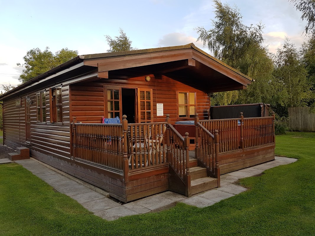 Wooden holiday lodge with a porch, surrounded by greenery and a clear sky in Sutton upon Derwent, Yorkshire.