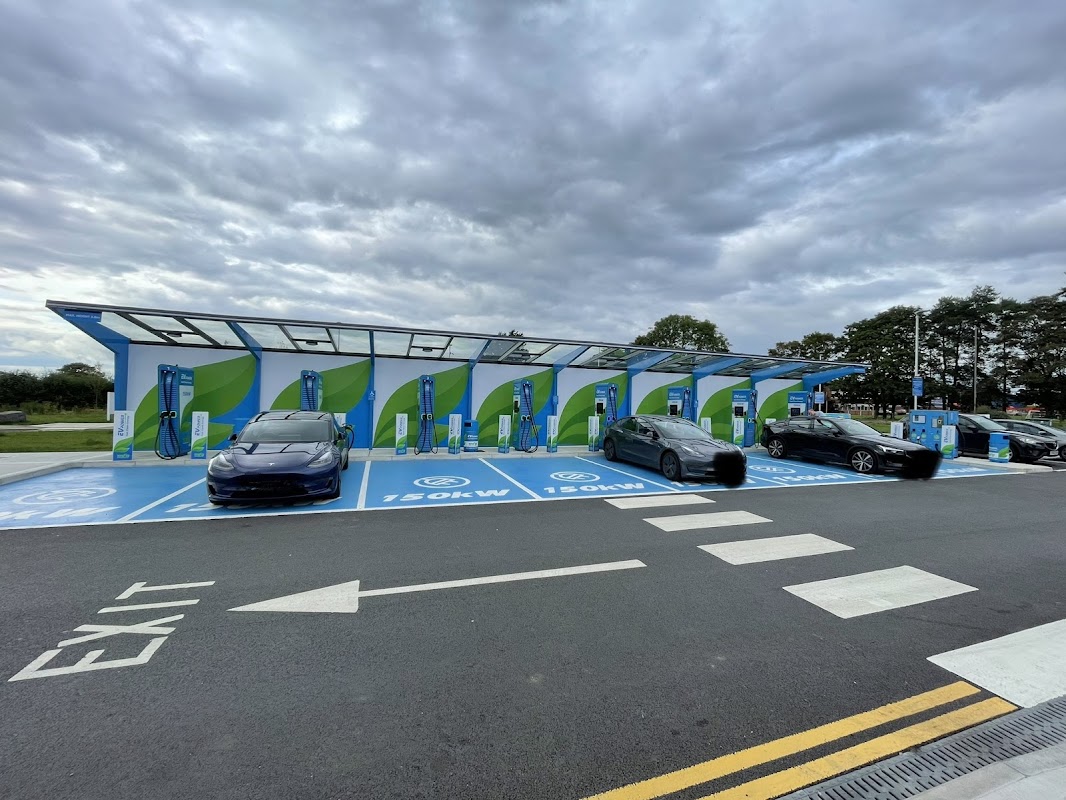 MFG Charging Station with multiple electric vehicle chargers and parked cars under a cloudy sky in Thirsk, Yorkshire.