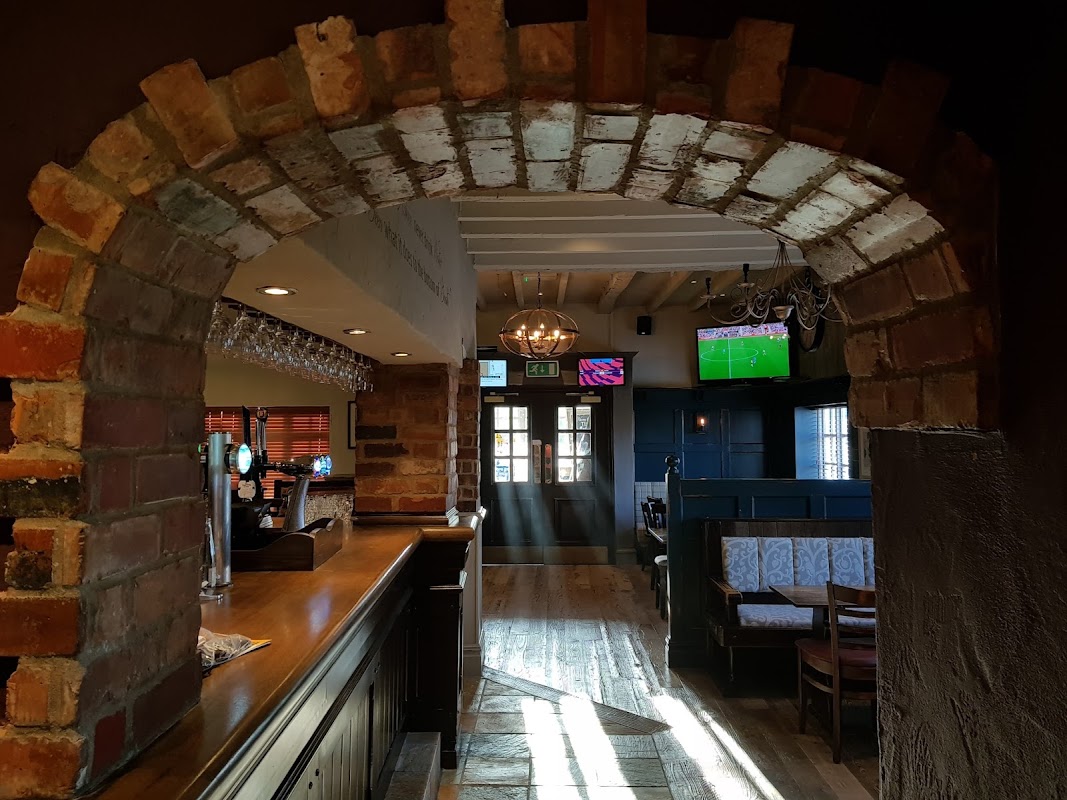 Brick archway leading to a cozy pub interior with wooden floors, bar, and TVs showing sports.