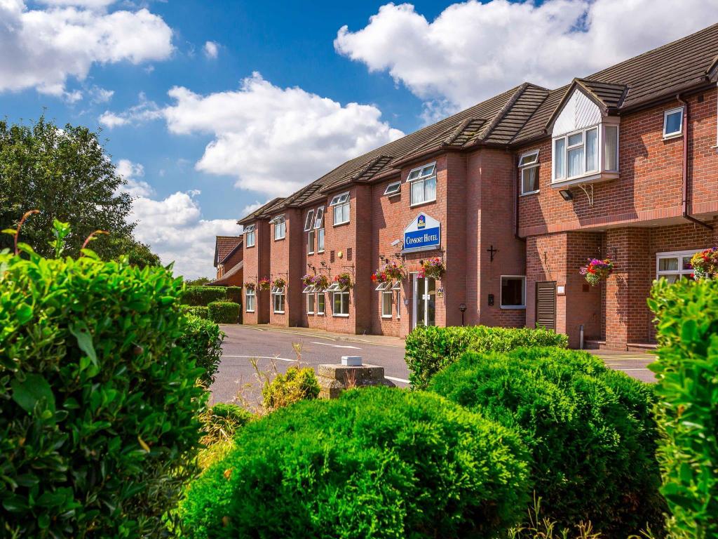 Brick building with blue signage, surrounded by neatly trimmed hedges and colorful flower baskets under a bright sky.