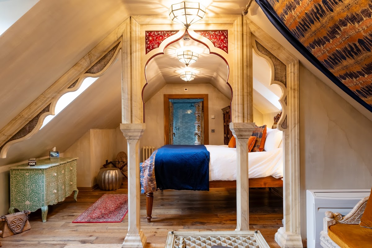 Stylish attic room with ornate arches, wooden flooring, a large bed, and decorative furnishings in a cozy ambiance.