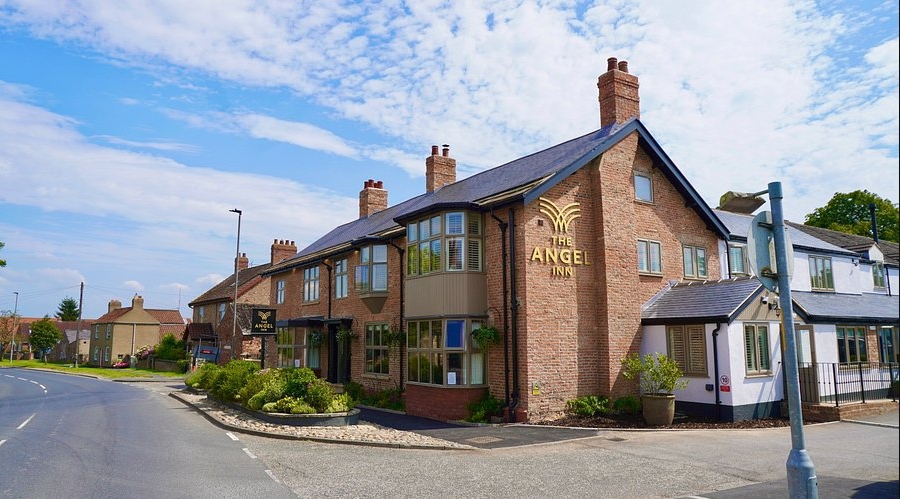 The Angel Inn at Topcliffe, a brick building with a sign, surrounded by greenery and a clear blue sky.
