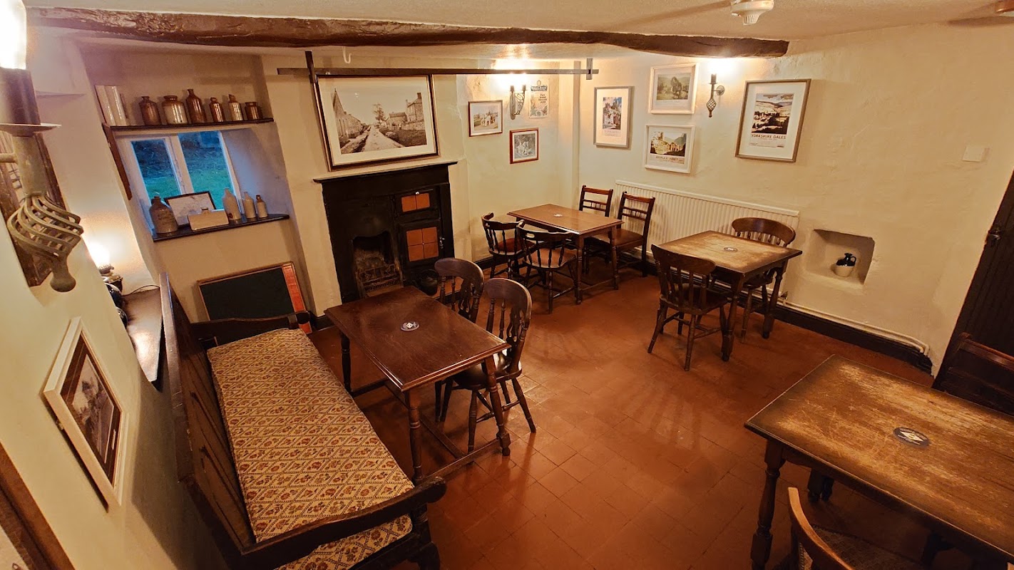 Cozy bar interior with wooden tables, chairs, a fireplace, and framed artwork on the walls.