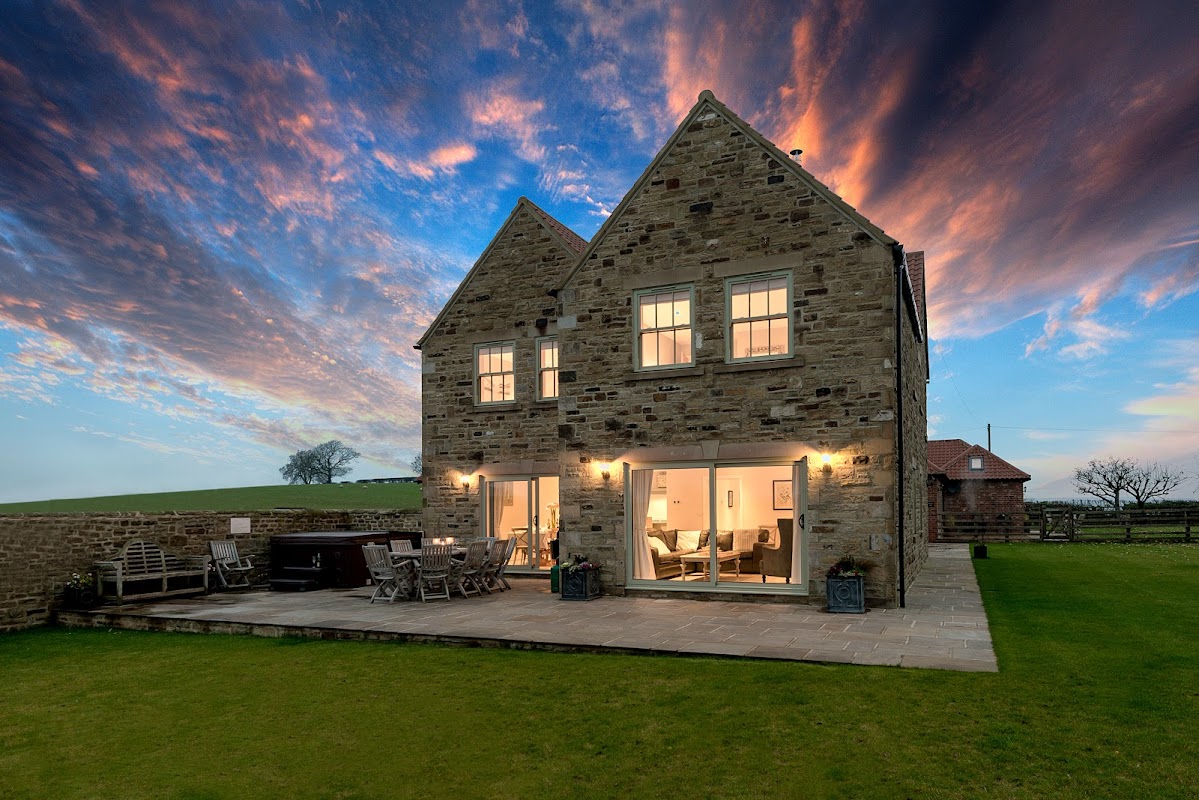 Stone farmhouse with large windows, patio area, and scenic sky at dusk in Tunstall, North Yorkshire.
