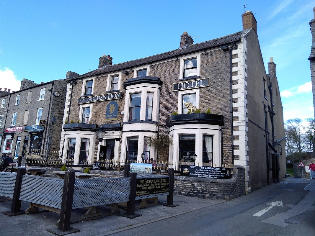 Historic stone building with "Golden Lion Hotel" signage, featuring a lion statue and outdoor seating area.