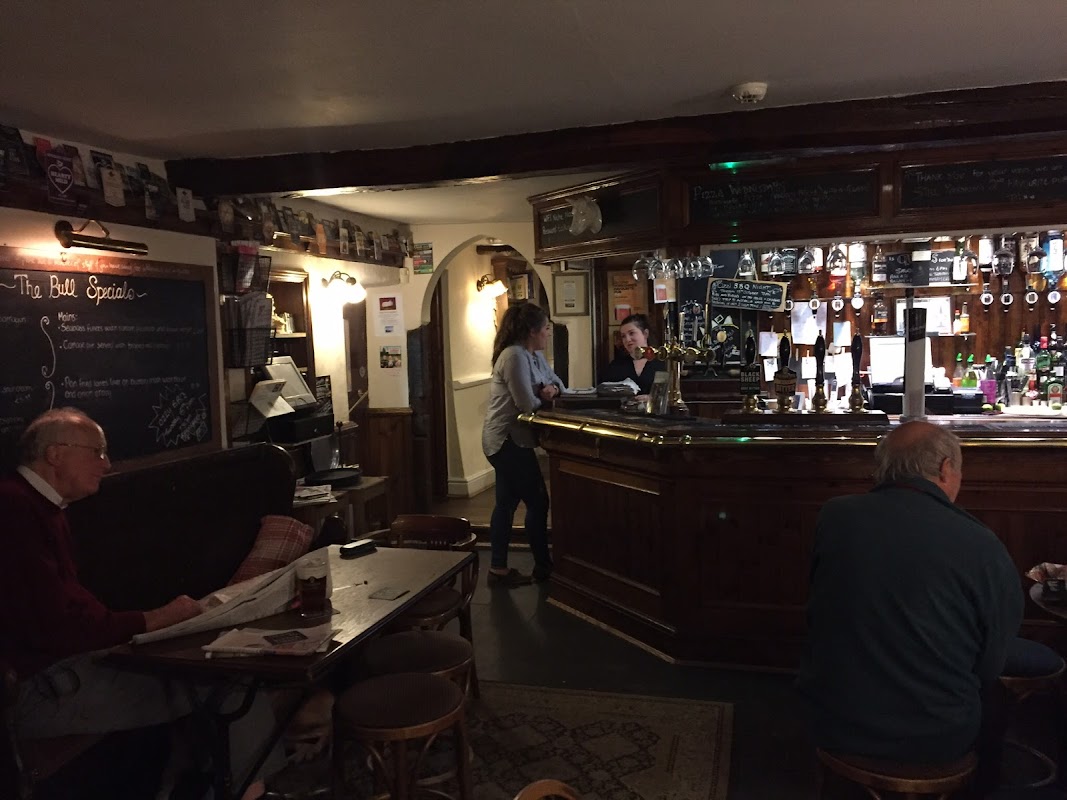 Cozy interior of The Bull Inn, featuring a wooden bar, patrons seated, and a chalkboard displaying specials.