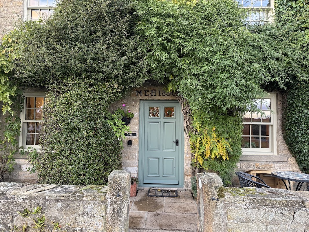 Charming stone farmhouse entrance, adorned with lush greenery and a light blue door, surrounded by a quaint stone wall.