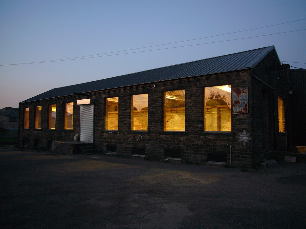 Brick building with large illuminated windows, featuring a metal roof, set against a twilight sky.