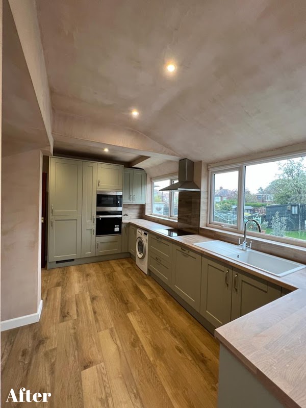 Modern kitchen with light wood flooring, gray cabinets, stainless steel appliances, and large windows overlooking greenery.