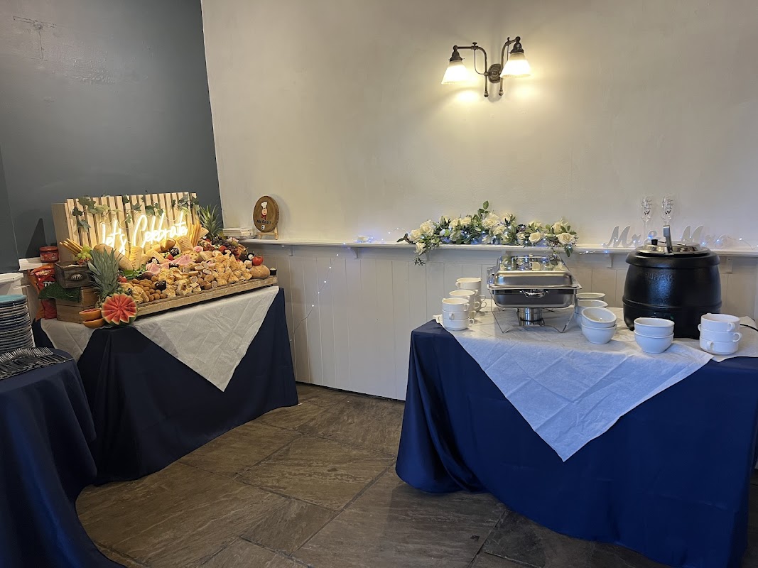 Buffet setup with decorative food display, silver serving trays, and white tablecloths in a cozy bar setting.