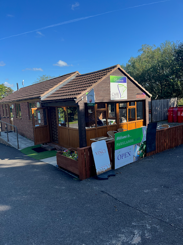 Cozy cafe with wooden exterior, green signage, and outdoor seating in Yafforth, Yorkshire, surrounded by trees.