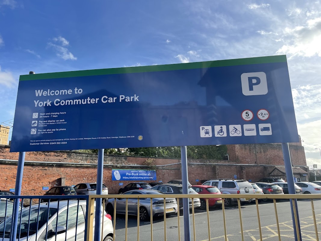 Welcome sign for York Commuter Car Park with parking details, hours, and contact information. Cars visible in foreground.