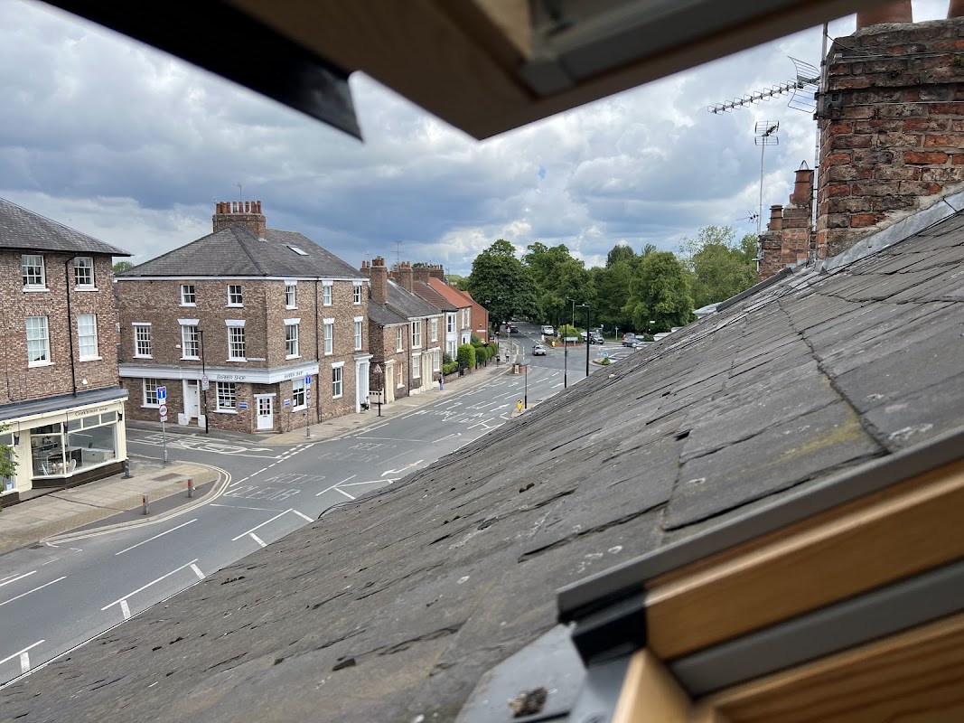 View from a roof window showing brick buildings, a street, and greenery in York, Yorkshire under a cloudy sky.