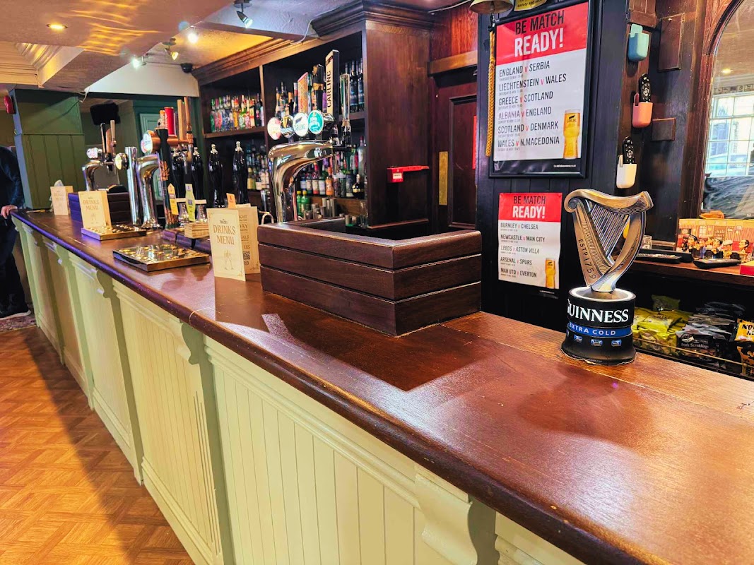 Wooden bar with taps, drinks, and a Guinness can; match day promotions displayed on a sign.
